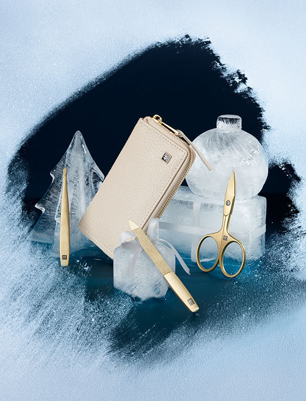 Vereiste an einer Stelle freigekratzt. Hier sind ein beiges Etui und goldene Maniküreprodukte, arrangiert auf weihnachtlichen Eisfiguren vor dunkelblauem Hintergrund.