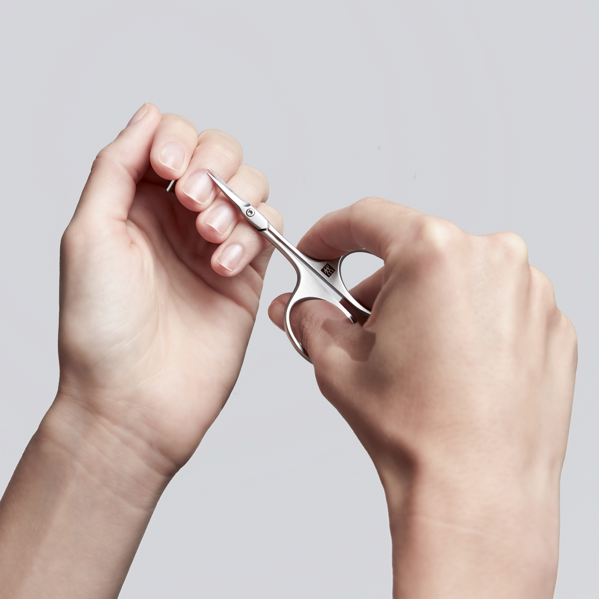 Anwendung einer ZWILLING Premium Nagelhautschere mit Turmspitze aus rostfreiem Edelstahl an der Nagelhaut des linken Mittelfingers.