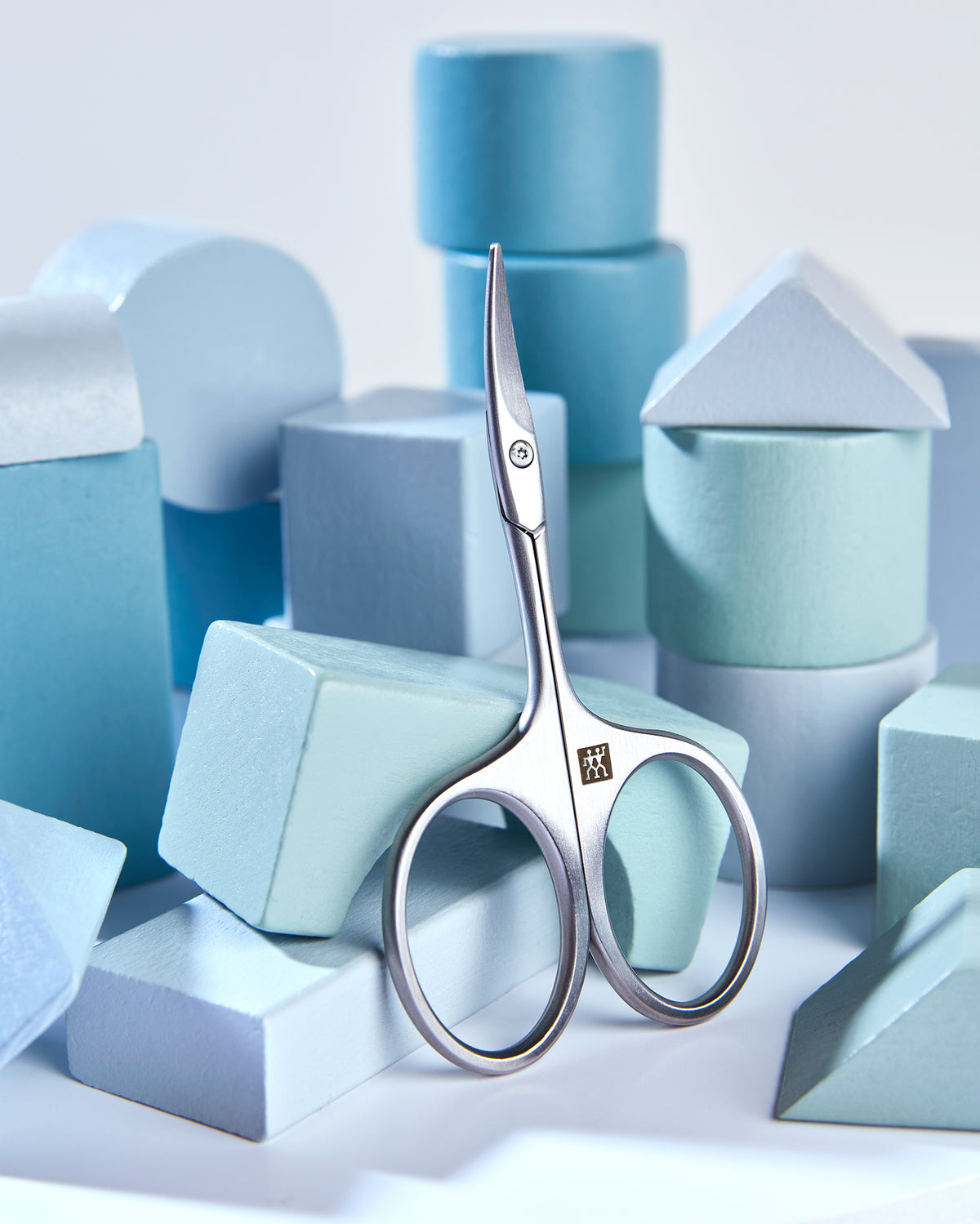 Sehr hochwertige Darstellung der ZWILLING Premium Baby-Nagelschere inmitten von blauen, verspielten Holzobjekten.